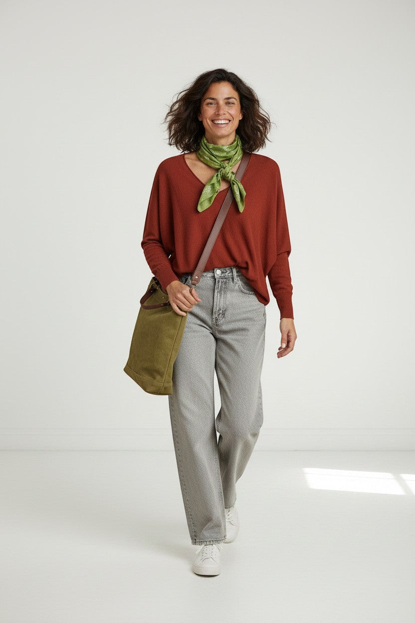 Calendula-shop Abril rust red V-neck sweater worn by a smiling woman with a green neck scarf and grey jeans