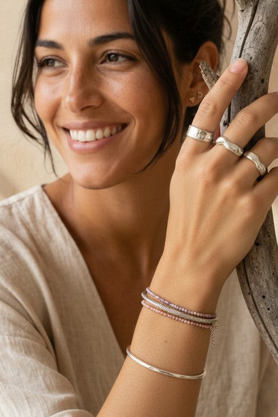 Mujer sonriente luciendo un anillo ancho troquelado de plata de ley 925 de Calendula-shop en un entorno natural