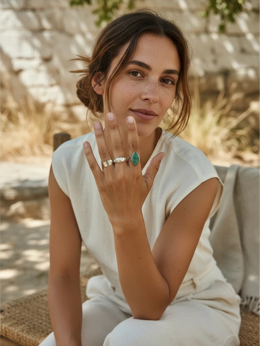 Mujer luciendo un anillo de esmeralda natural de Calendula-shop junto a otros anillos de plata en su mano
