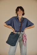 Calendula-shop blue canvas tote bag with brown leather straps worn crossbody by a smiling woman in a blue shirt
