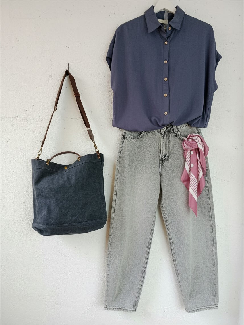 Calendula-shop blue canvas tote bag with brown leather handles hanging on a white wall next to an outfit