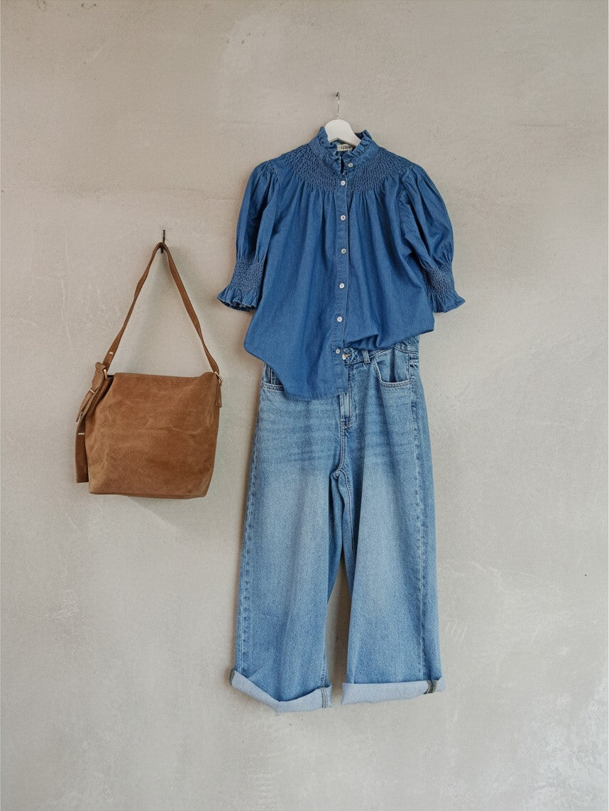 Calendula-shop blue cotton short-sleeve blouse with gathered neck and cuffs, paired with jeans and a brown bag.