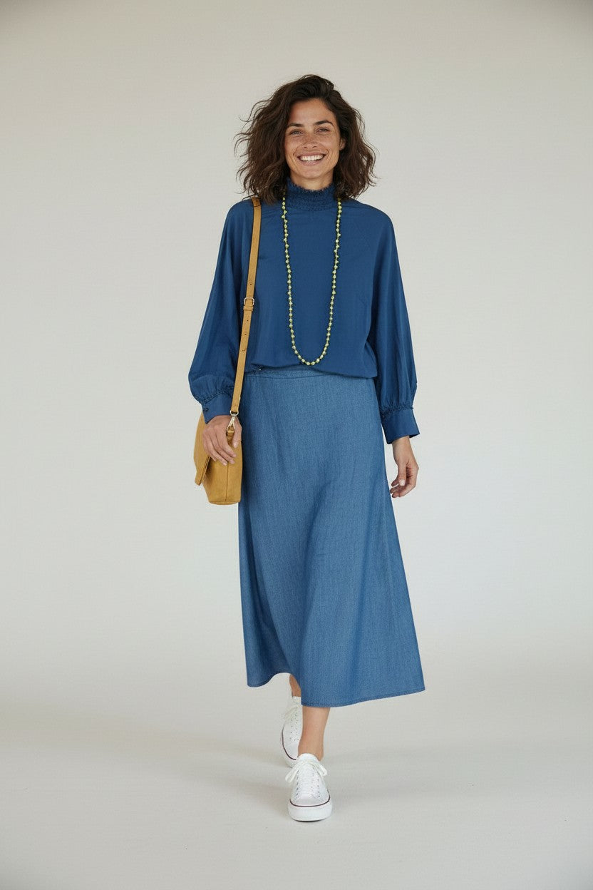 Calendula-shop blue long-sleeve cotton blouse with a gathered high neck, worn by a smiling woman.
