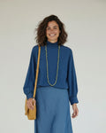 Calendula-shop blue long-sleeve cotton blouse with gathered high neck, worn by a smiling woman with a midi skirt.