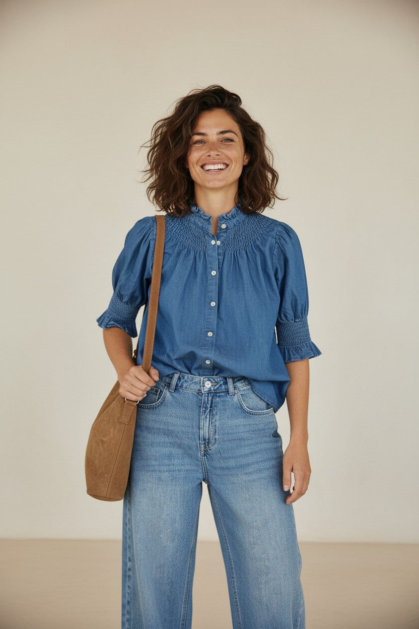 Calendula-shop blue denim short-sleeve blouse with ruffled collar and smocked details worn by a smiling woman