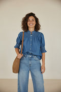 Calendula-shop blue denim short-sleeve blouse with ruffled collar and smocked details worn by a smiling woman