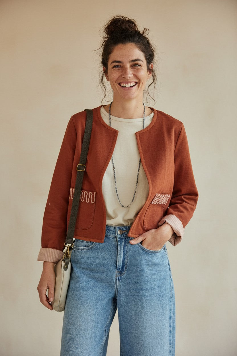 Modelo sonriente vistiendo la chaqueta corta Julia de Calendula-shop en color teja con detalles bordados en bolsillos