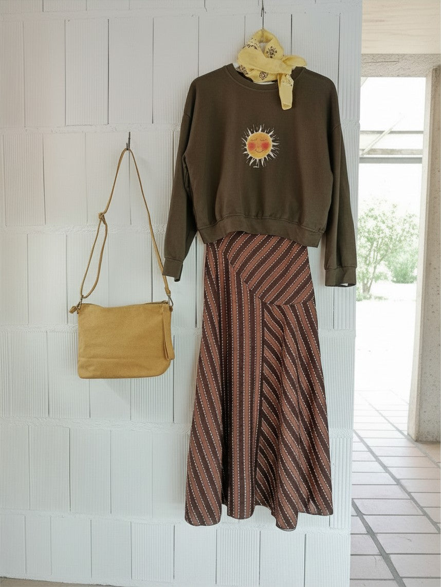 Calendula-shop chocolate brown cropped sweatshirt with exclusive sun graphic, styled with a striped skirt and bag.