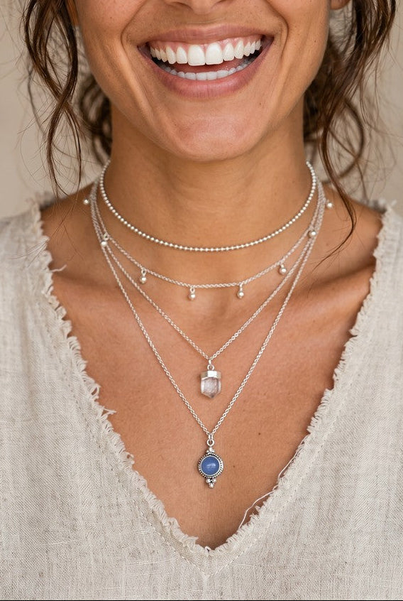Mujer sonriente luciendo el colgante Eter de Calendula-shop con piedra de calcedonia azul oscuro y cadena de plata.