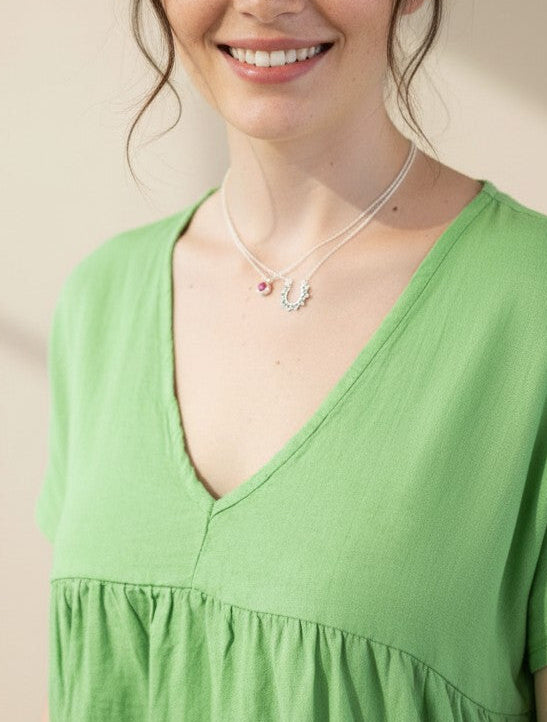 Modelo sonriente con collar Calendula-shop de plata de ley y piedra natural fucsia sobre blusa verde