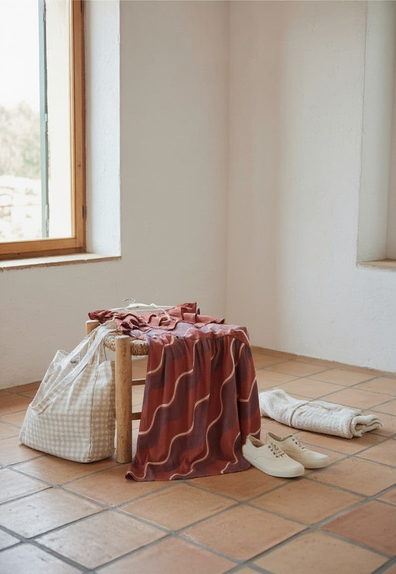 Falda larga Calendula-shop de ondas en tonos rojizos, fluida y cómoda, sobre una silla de madera en un entorno rústico