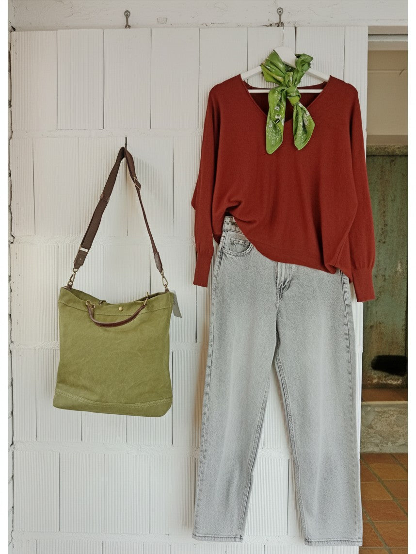 Calendula-shop green canvas tote bag with brown leather handles hanging next to a red sweater and light wash jeans
