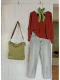 Calendula-shop green canvas tote bag with brown leather handles hanging next to a red sweater and light wash jeans