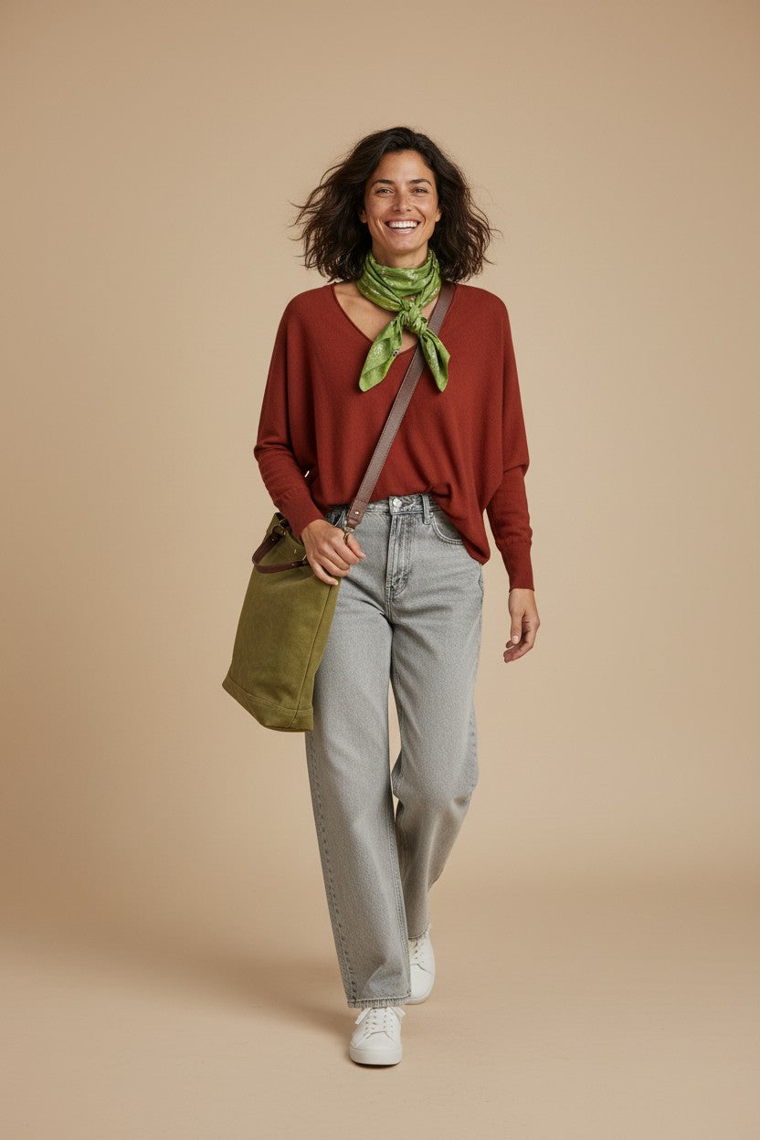 Calendula-shop green canvas tote bag with brown straps worn by a smiling woman in a rust sweater and grey jeans
