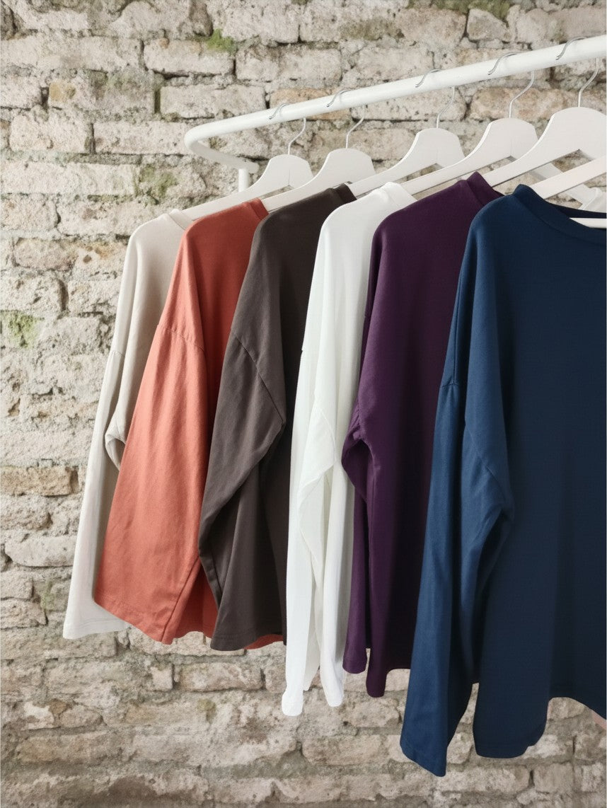 Calendula-shop Marta long sleeve cotton shirts in various colors hanging on a rack against a rustic brick wall