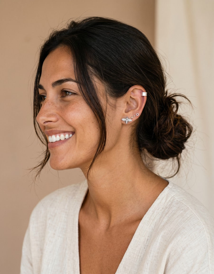 Modelo luciendo pendientes mini de Calendula-shop con forma de abeja y aros en la oreja sobre fondo neutro.