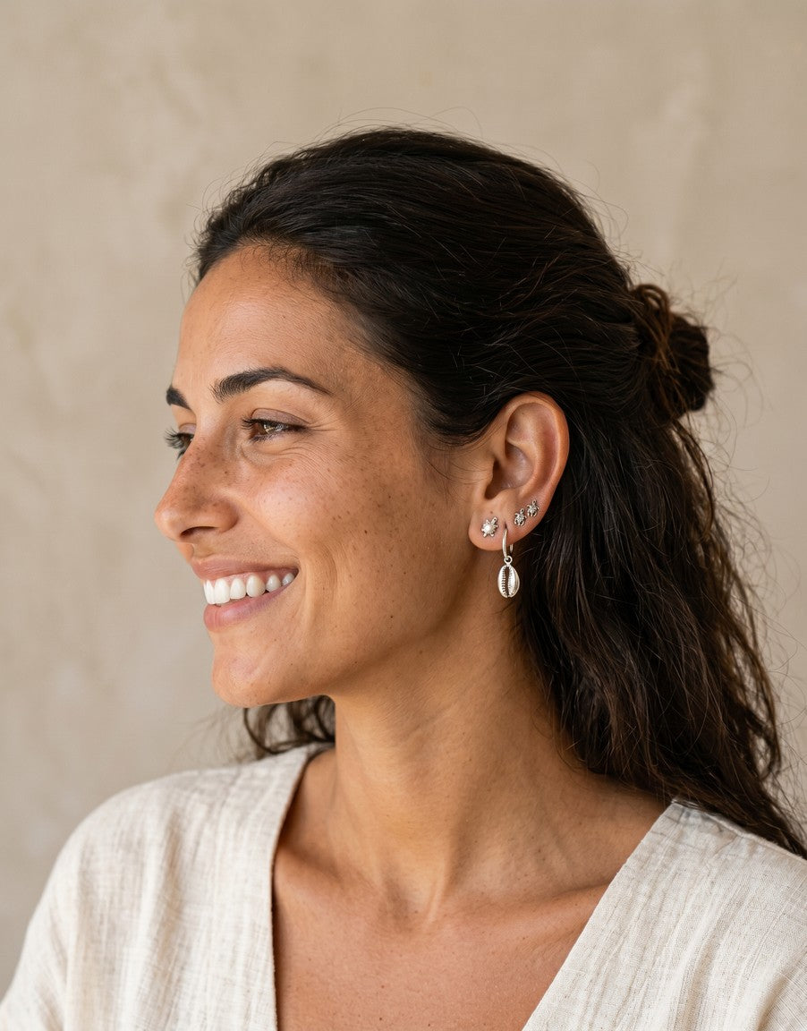 Modelo sonriendo luciendo pendientes mini de Calendula-shop con formas de estrella, luna y concha en plata