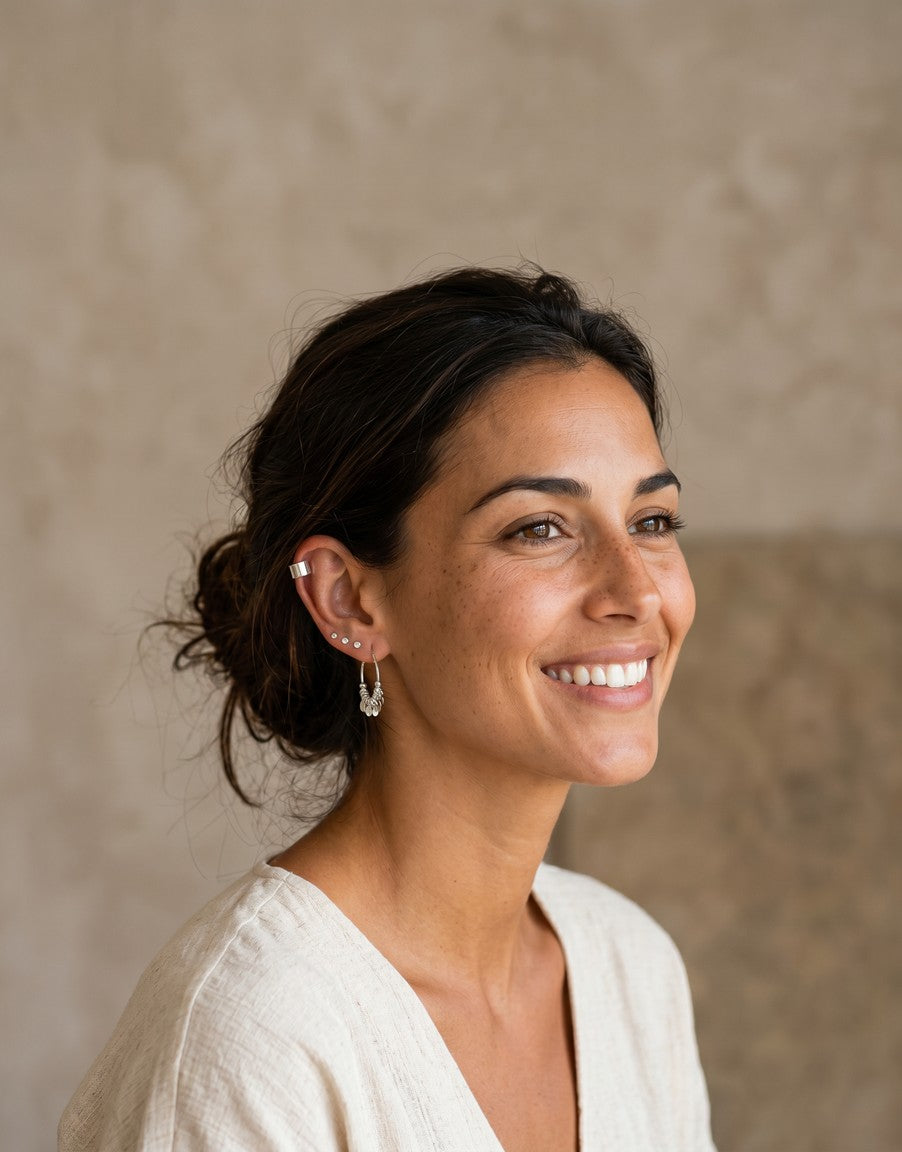 Mujer sonriente luciendo pendientes mini de plata de ley de Calendula-shop, incluyendo aros y pendientes de presión.