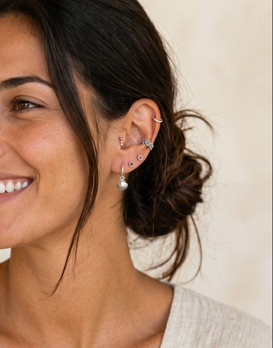 Mujer sonriente luciendo pendientes mini de plata de ley de Calendula-shop en diferentes formas geométricas