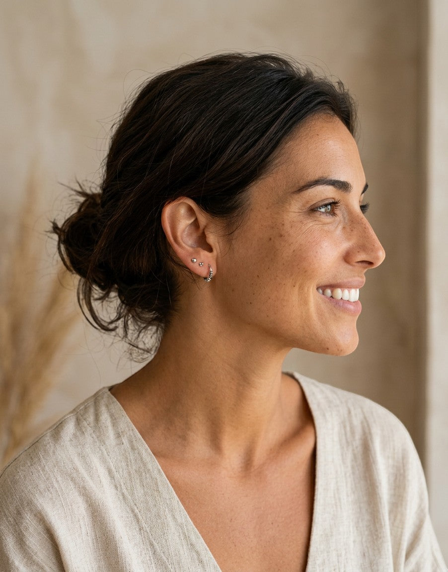 Mujer sonriente luciendo pendientes mini de plata de ley 925 de Calendula-shop en su oreja