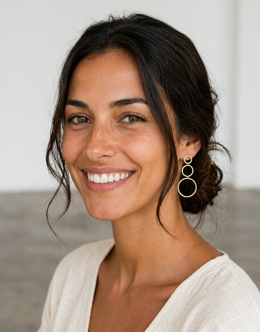 Pendientes Calendula-shop de plata de ley 925 con tres círculos dorados en cascada lucidos por una modelo sonriente.
