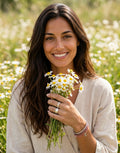 Mujer sonriente en campo de flores luciendo pulsera rígida de plata de ley 925 de Calendula-shop con líneas labradas.