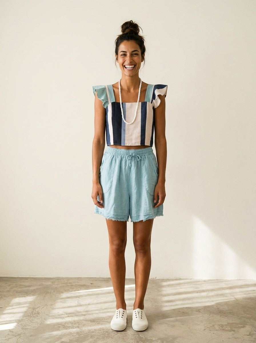 Modelo sonriente vistiendo el top Inés de Calendula-shop con rayas verticales, volantes en hombros y shorts celestes