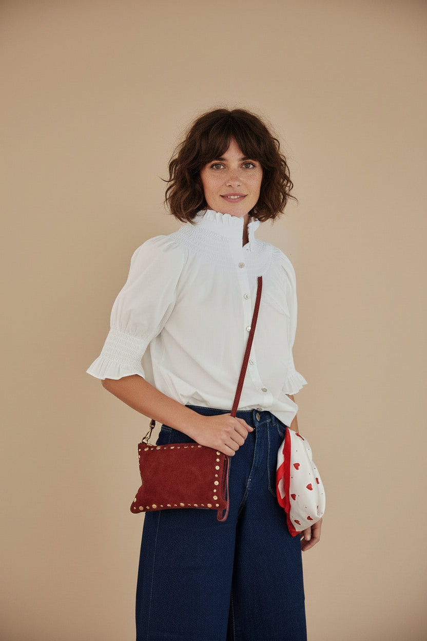 Calendula-shop white short-sleeve blouse with gathered high neck and ruffled cuffs worn with a red suede crossbody bag